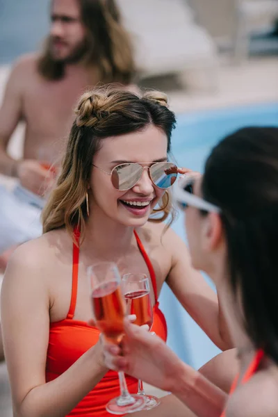 Selective focus of young female friends drinking champagne and smiling at pool — Stock Photo