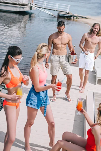 Vista de ángulo alto de los jóvenes que beben bebidas refrescantes en la playa - foto de stock