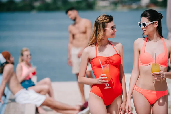 Hermosas chicas en traje de baño celebración de cócteles de verano y mirándose en la playa - foto de stock