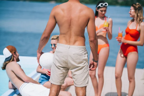 Vue arrière de l'homme tenant le ballon et passant du temps avec des amis au bord de la piscine — Photo de stock