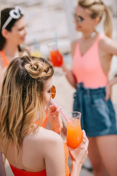 Jovem mulher bebendo coquetel de verão enquanto passa tempo com namoradas na praia — Fotografia de Stock