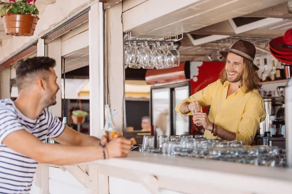 Camarero sonriente y cliente con botella de cerveza mirándose en el bar de la playa — Stock Photo