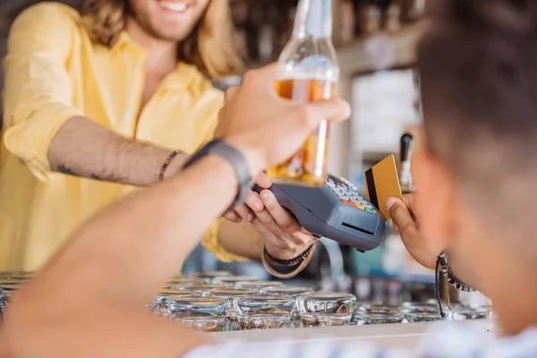 Куповані постріл молодий чоловік тримає пляшку пива та оплати кредитною карткою в барі на пляжі — стокове фото