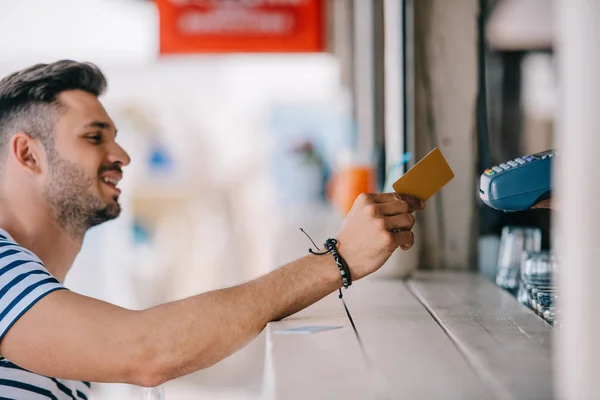 Vue latérale du jeune homme souriant payant par carte de crédit au bar de la plage — Photo de stock