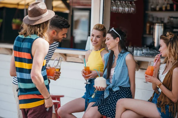 Felici giovani uomini e donne che parlano e bevono cocktail al bar sulla spiaggia — Foto stock