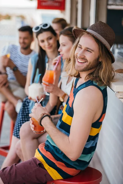 Joven guapo sonriendo y bebiendo cóctel de verano en el bar de la playa - foto de stock