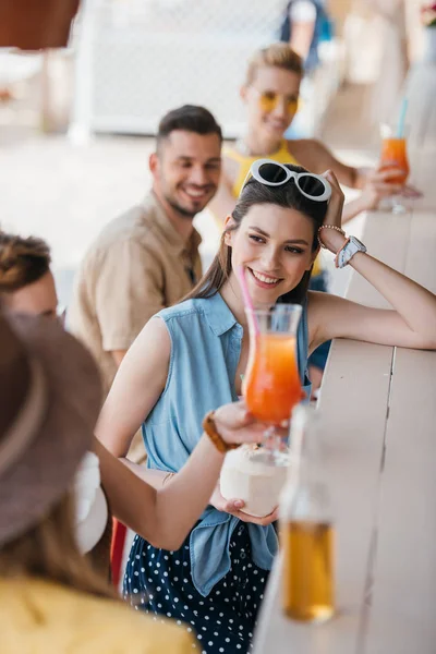 Lächelnde junge Frau trinkt Sommercocktail mit Freunden an der Strandbar — Stockfoto