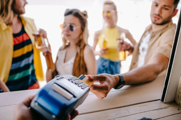 Recortado disparo de joven que paga con tarjeta de crédito y terminal de pago en el bar de la playa - foto de stock