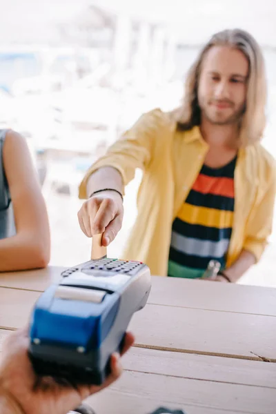 Foco seletivo do jovem pagando com cartão de crédito no terminal no bar da praia — Fotografia de Stock