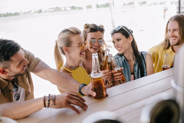 Избирательный фокус улыбающихся молодых друзей, пьющих пиво вместе в баре на пляже — стоковое фото