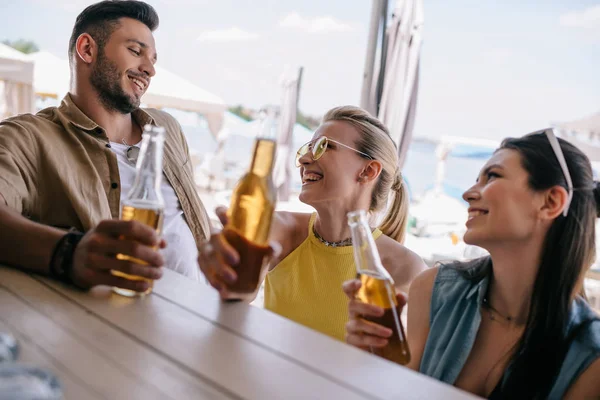 Happy young man looking at beautiful smiling girls and drinking beer together at beach bar — Stock Photo