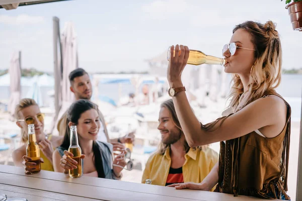 Felices jóvenes amigos y amigas bebiendo cerveza en el bar de la playa - foto de stock