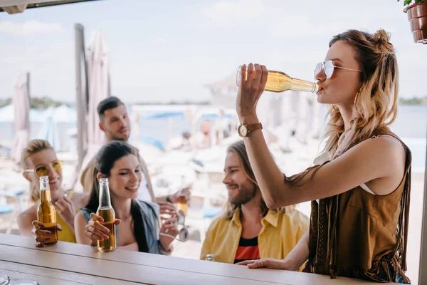 Happy young male and female friends drinking beer at beach bar — Stock Photo