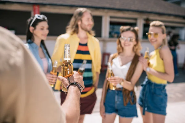 Plan recadré d'un homme tenant une bouteille de bière près d'amis buvant de la bière au bar de la plage — Photo de stock