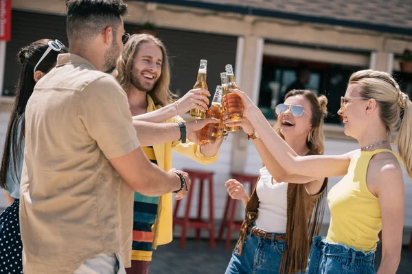 Happy young people clinking beer bottles at beach bar — Stock Photo