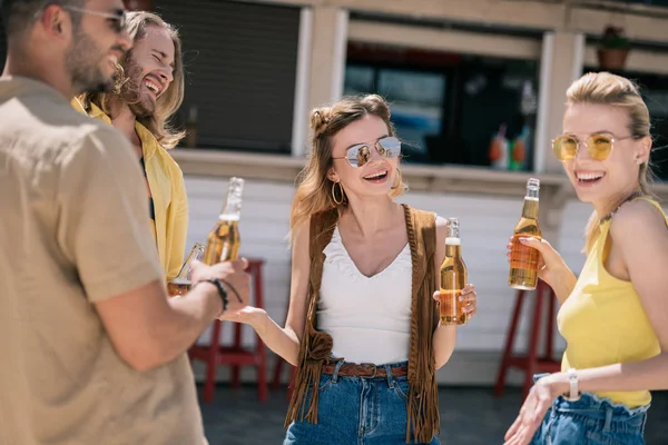 Улыбающиеся молодые люди пьют пиво и разговаривают в пляжном баре — стоковое фото