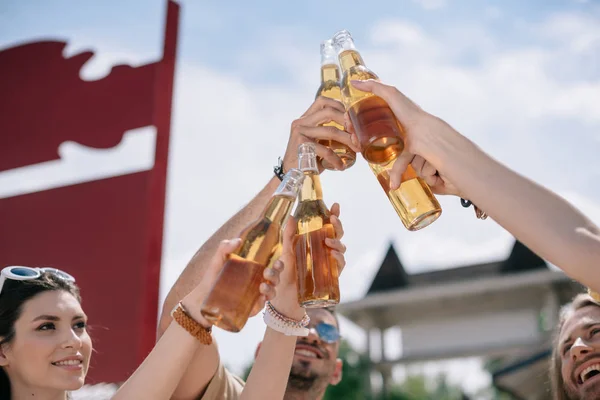 Smiling young people clinking beer bottles at summer day — Stock Photo