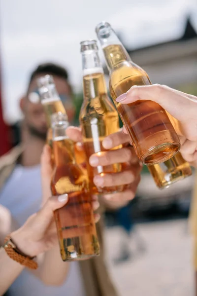 Partial view of young people clinking beer bottles outdoors — Stock Photo