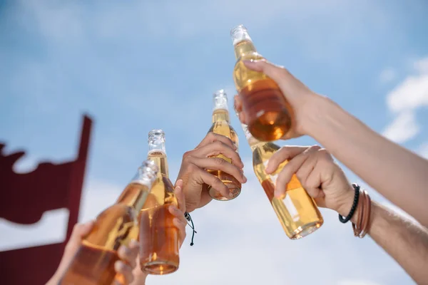 Cropped shot of young people clinking beer bottles outdoors — Stock Photo