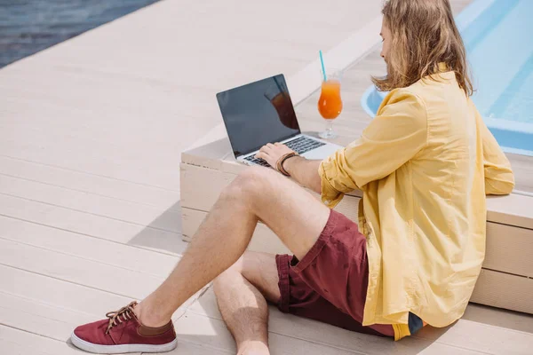 Jovem usando laptop com tela em branco enquanto sentado à beira da piscina — Fotografia de Stock