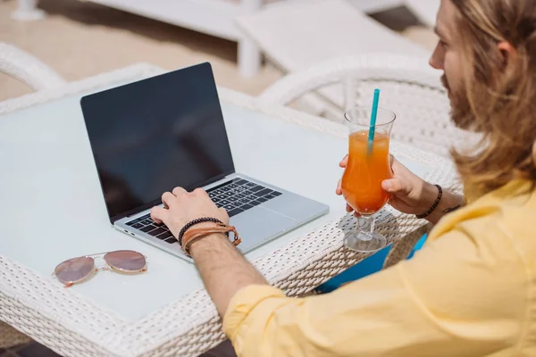 Plan recadré de l'homme tenant cocktail et en utilisant un ordinateur portable avec écran blanc à l'extérieur — Photo de stock