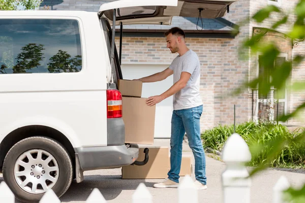 Side view of young man moving boxes from car into new house — Stock Photo