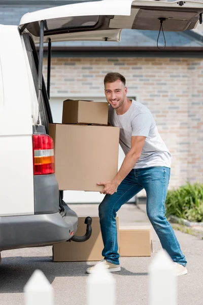 Lächelnder junger Mann zieht Kisten aus Auto in neues Haus — Stockfoto