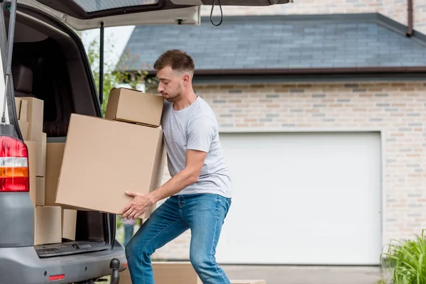 Faticoso giovane uomo che muove scatole da auto in nuova casa — Foto stock