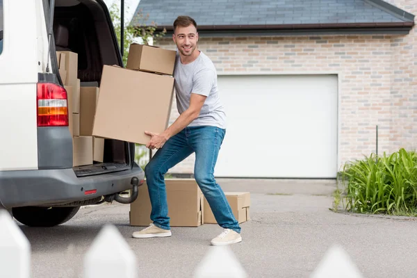 Young smiling man moving boxes from car into new house — Stock Photo