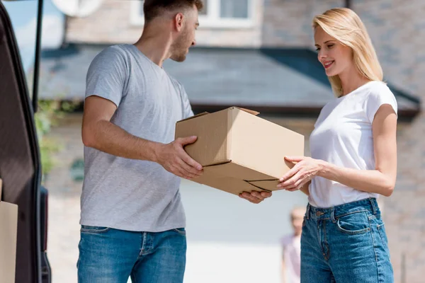 Hombre dando caja de cartón a la esposa mientras su hija de pie detrás en el patio de la nueva casa - foto de stock