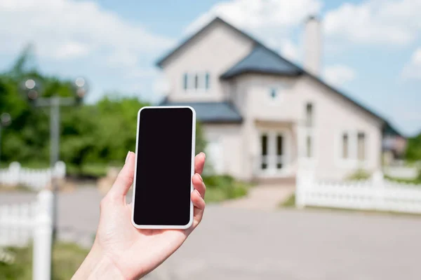 Cropped image of young woman holding smartphone with blank screen in front of house — Stock Photo