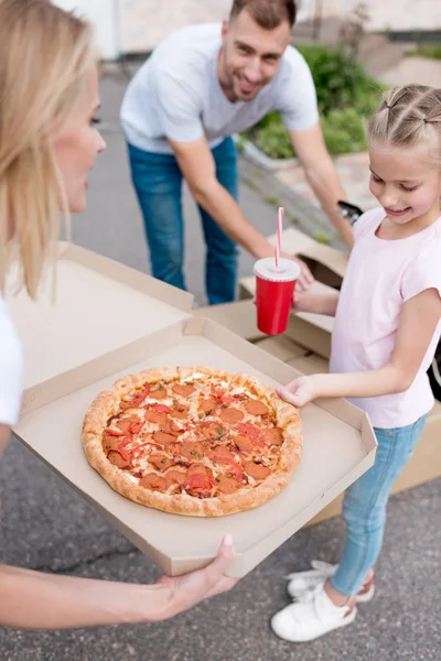 Mother holding box with pizza and daughter taking slice of pizza while father unpacking cardboard boxes — Stock Photo