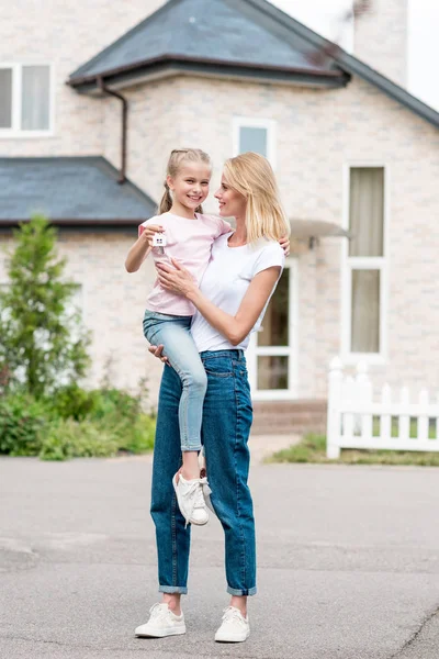 Femme tenant une petite fille avec la clé à la main devant une nouvelle maison — Photo de stock