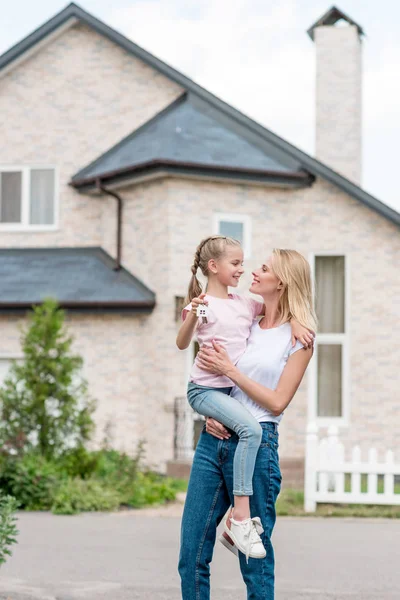 Smiling woman holding little daughter with key from new cottage — Stock Photo