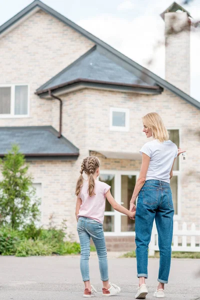 Vista trasera de la pequeña hija con la madre cogida de la mano en frente de la nueva casa — Stock Photo