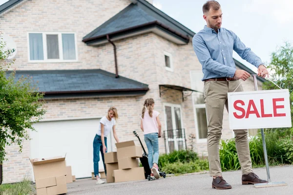 Agent immobilier masculin accrochant signe de vente en face de personnes déménageant de la maison — Photo de stock
