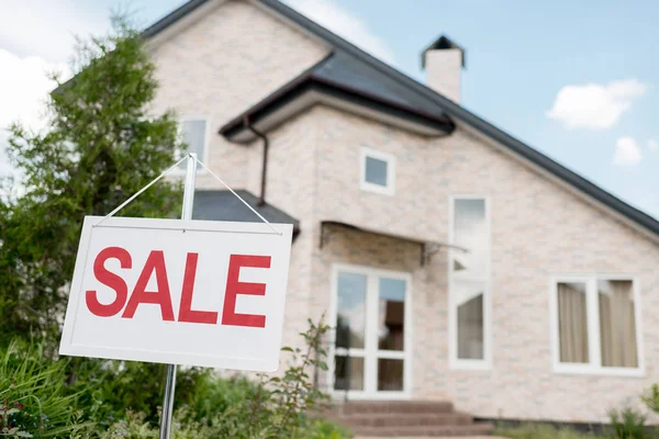 Close up shot of wooden placard with sale sign in front of modern cottage — Stock Photo