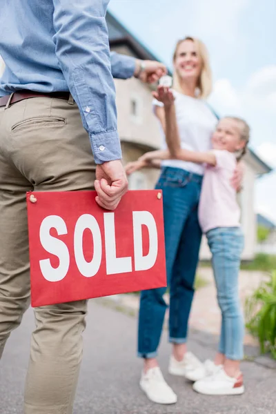 Geschnittenes Bild eines Maklers mit verkauftem Schild, der einer jungen Frau mit Tochter den Schlüssel vor dem neuen Haus übergibt — Stockfoto