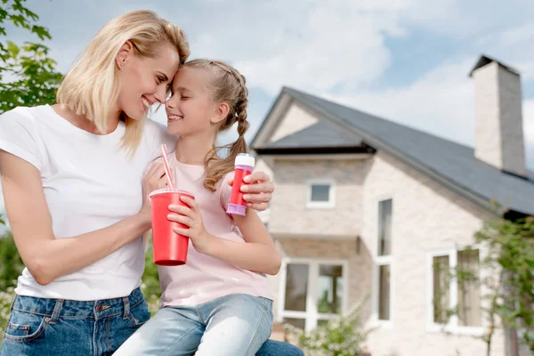Femme heureuse assis front au front avec fille et tenant ventilateur à bulles en face de la nouvelle maison — Photo de stock