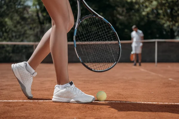 Cropped shot of woman with racket standing over tennis ball lying on court — Stock Photo
