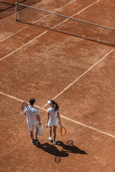 Visão de alto ângulo de casal esportivo com raquetes andando por quadra de tênis — Fotografia de Stock