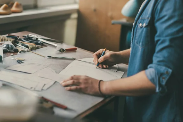 Partial view of cobbler in denim shirt drawing outline for shoes at workshop — Stock Photo