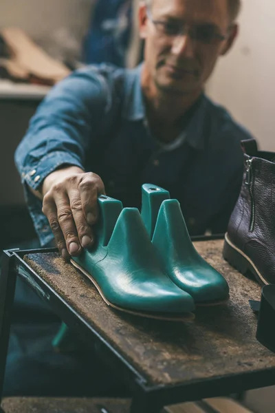 Selective focus of shoemaker holding footwear workpieces from shelf in workshop — Stock Photo