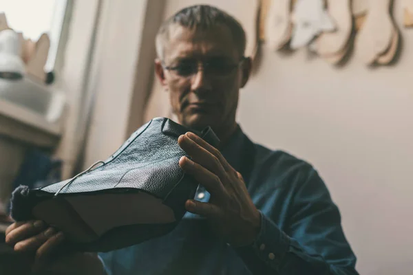 Mature shoemaker looking at unfinished leather boot — Stock Photo