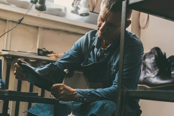 Zapatero maduro sosteniendo bota de cuero sin terminar en el taller - foto de stock