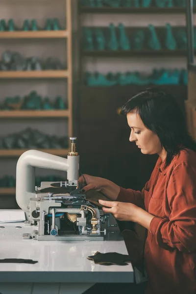Side view of middle aged seamstress working with sewing machine and leather at shoemaker workshop — Stock Photo