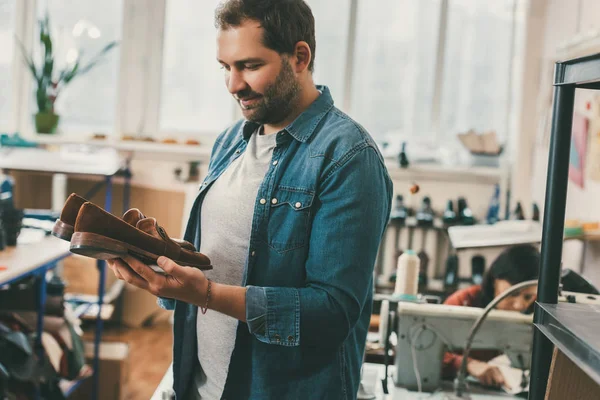 Shoemaker holding pair of finished shoes in cobbler's shop — Stock Photo