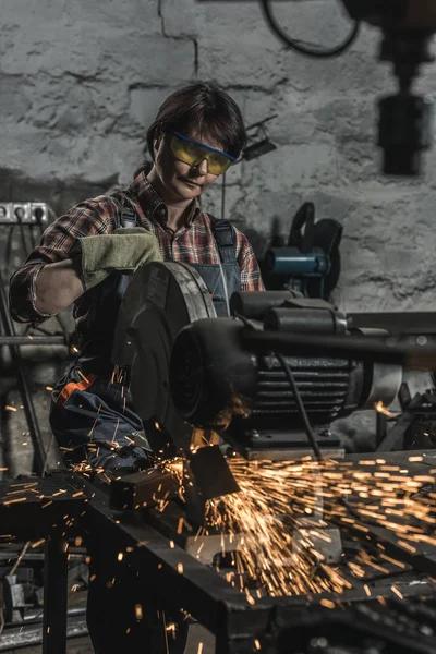 Soldador femenino en googles protectores usando linterna de soldadura en taller - foto de stock