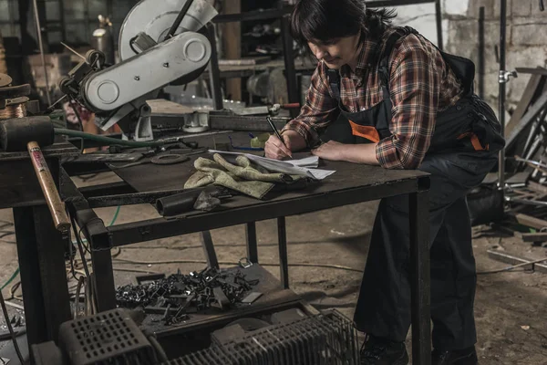 Female welder doing paperwork at table in workshop — Stock Photo