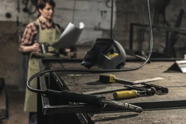 Selective focus of welder with cup of hot drink reading papers in workshop — Stock Photo